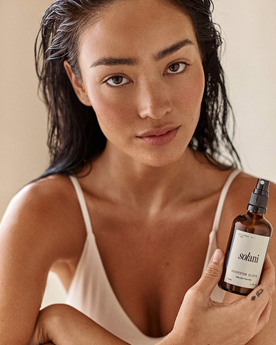 Model holding the Solani Ecosystem Elixir bottle against a warm neutral backdrop