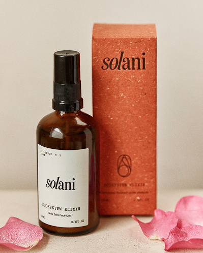 Solani Ecosystem Elixir bottle beside its terracotta carton, rose petals scattered around the base