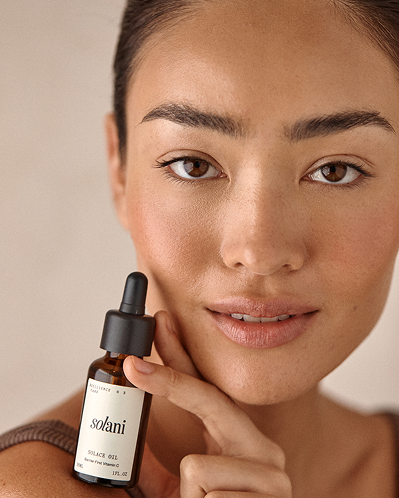 Model holding the Solani Solace Oil dropper bottle beside her chin