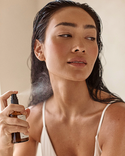Model misting Solani Ecosystem Elixir onto her face, fine spray visible in the air