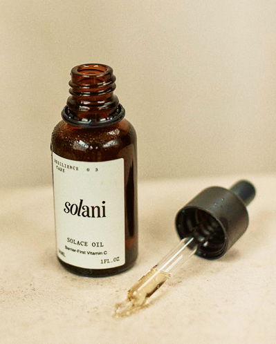 Open Solani Solace Oil bottle lying beside its glass dropper on a pale stone surface