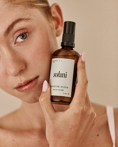 Model holding the Solani Ecosystem Elixir bottle beside her cheek