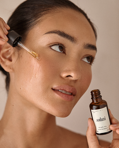 Model applying Solani Solace Oil to her cheek with the glass dropper