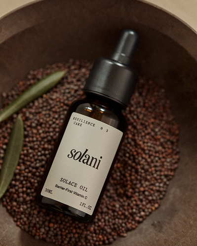 Solani Solace Oil bottle resting in a wooden bowl of seeds with a green sprig